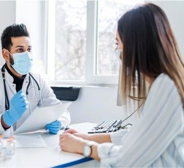 Doctor wearing a mask and gloves consulting with a patient in an office setting.